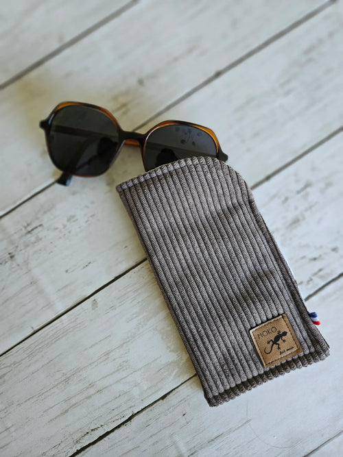 Étui à lunettes en velours côtelé gris avec lunettes de soleil sur fond bois clair
