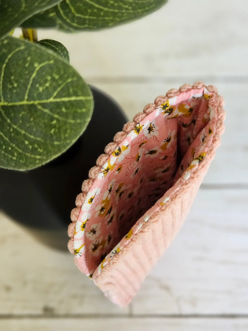 Pochette rose en tissu matelassé à fleurs, accessoire mode posé sur fond clair.