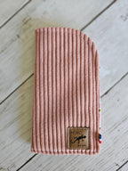 Étui à lunettes en velours côtelé rose, étiquette cuir, posé sur fond bois clair.