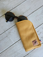 Étui à lunettes jaune côtelé en tissu sur fond bois, accessoire tendance avec lunettes de soleil.