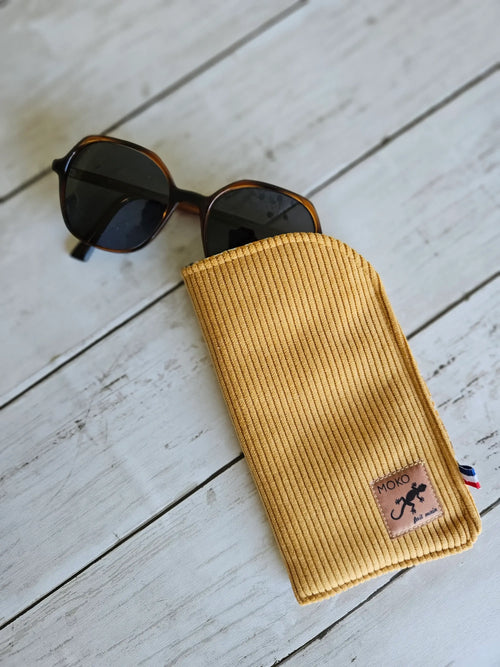 Étui à lunettes jaune côtelé en tissu sur fond bois, accessoire tendance avec lunettes de soleil.