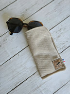Étui en tissu beige pour lunettes de soleil, accessoire mode posé sur fond bois clair