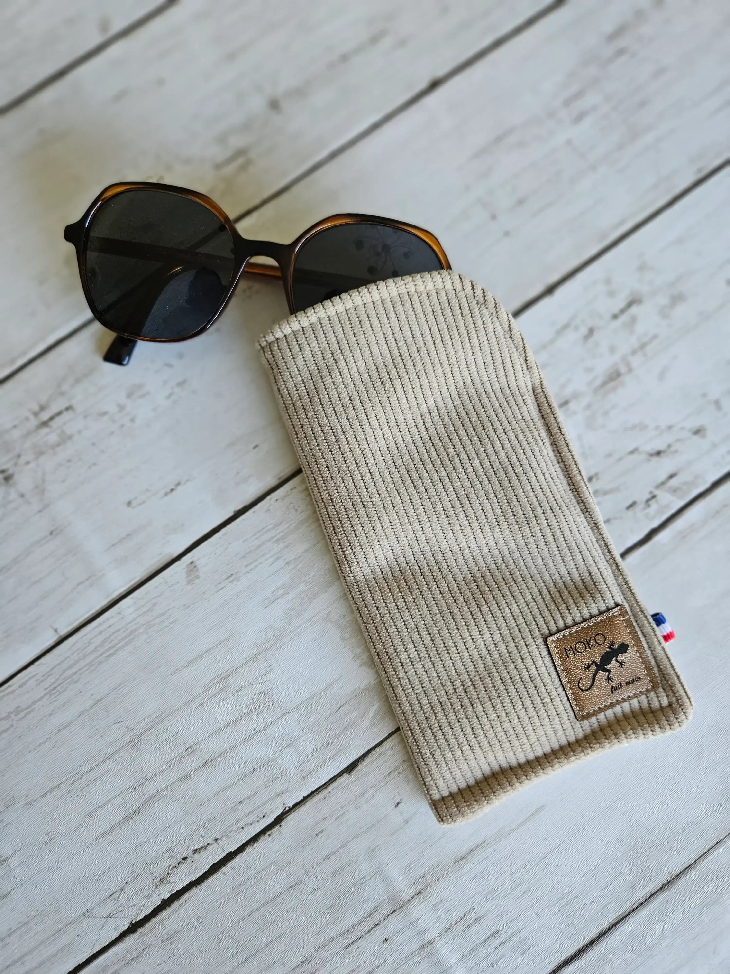 Étui en tissu beige pour lunettes de soleil, accessoire mode posé sur fond bois clair