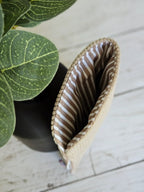 Pochette beige rayée marron, accessoire mode sur fond bois, près d'une plante