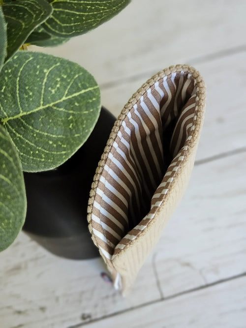 Pochette beige rayée marron, accessoire mode sur fond bois, près d'une plante