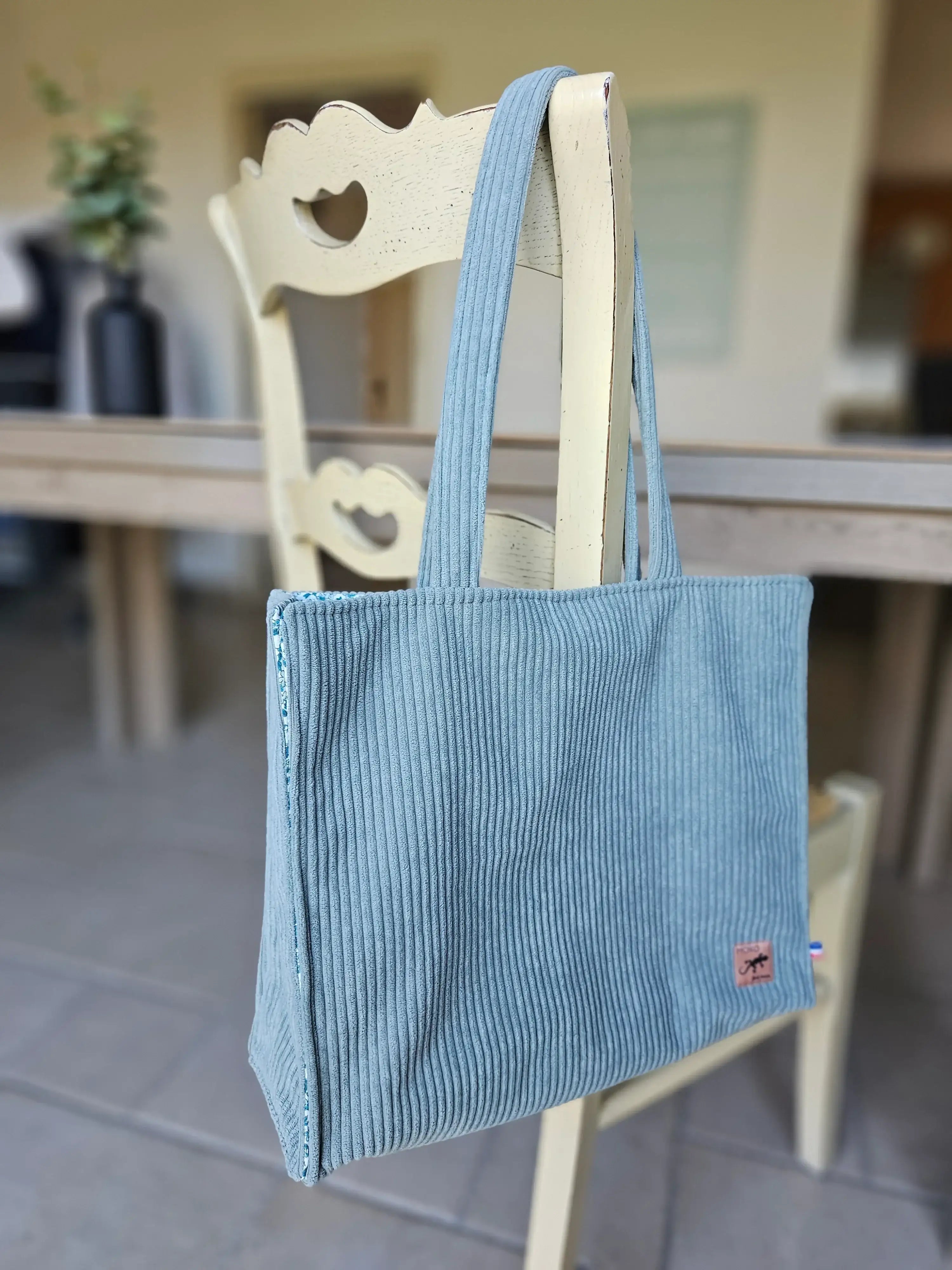 Sac cabas bleu en velours côtelé, posé sur une chaise, accessoire mode tendance.