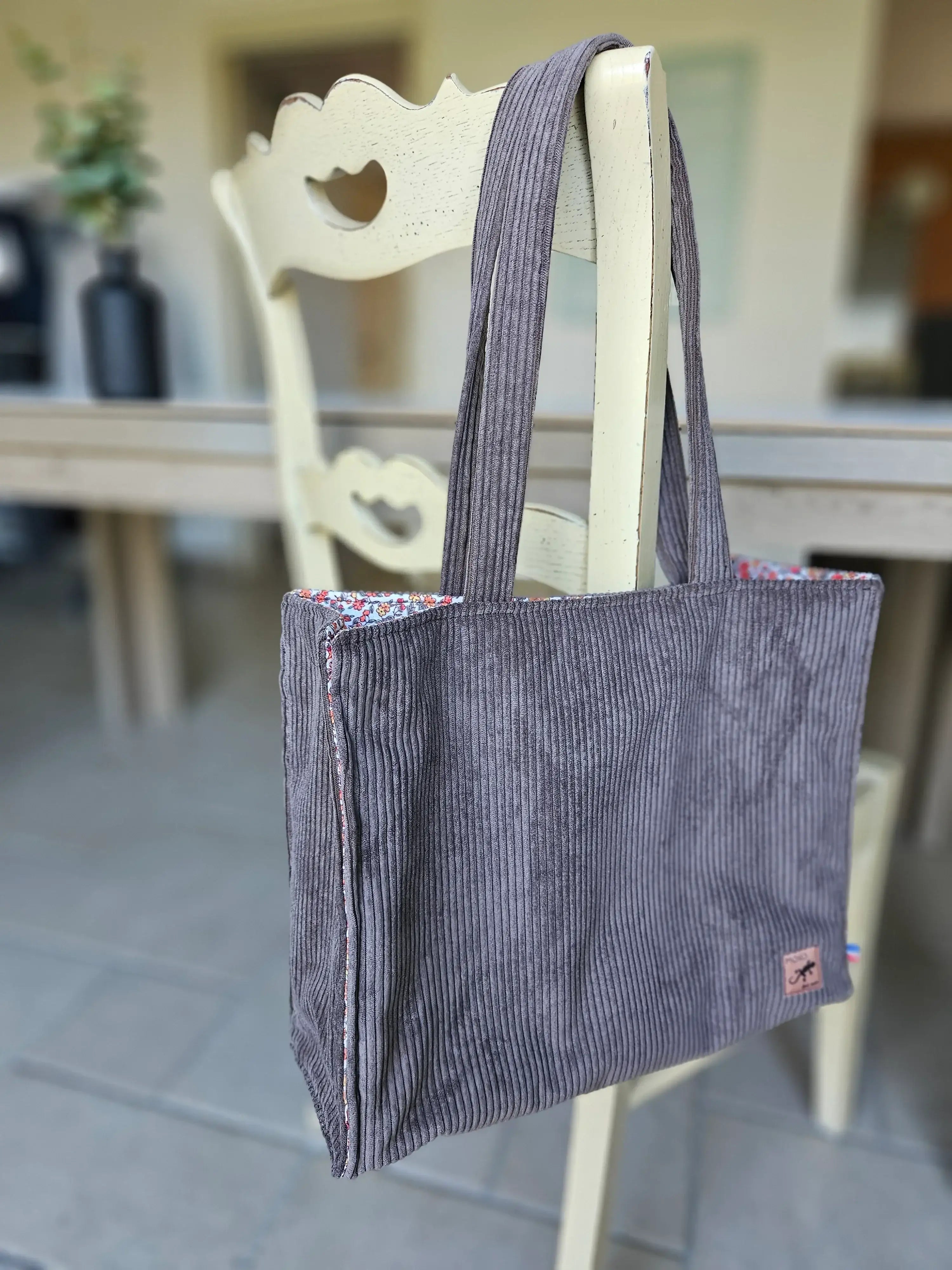 Sac cabas en velours côtelé gris suspendu à une chaise, accessoire mode tendance.