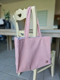 Sac cabas en tissu côtelé rose, suspendu à une chaise en bois, accessoires mode tendance.
