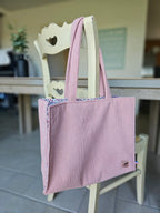 Sac cabas en tissu côtelé rose, suspendu à une chaise en bois, accessoires mode tendance.