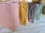 Quatre sacs cabas en velours côtelé pastel, posés sur une table en bois clair.