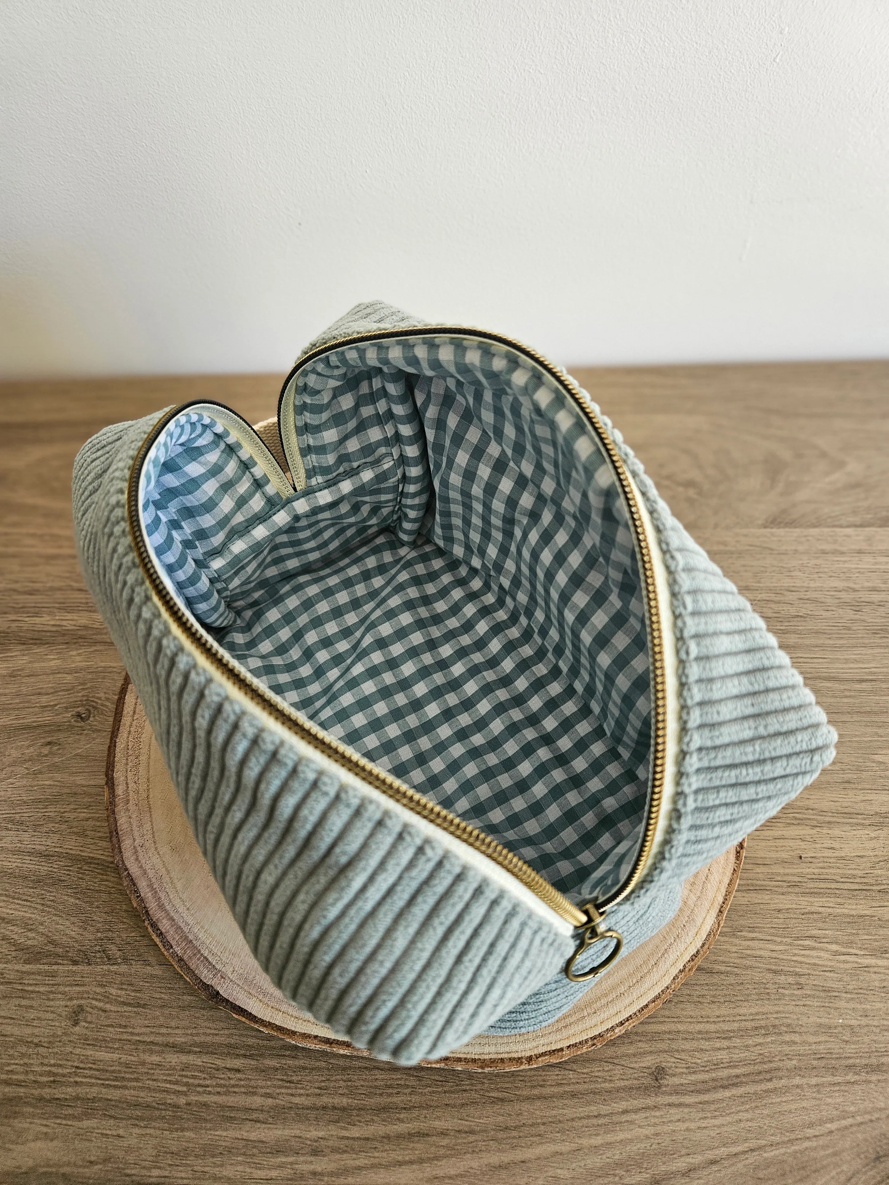 Pochette en velours côtelé vert ouverte, doublure intérieure à carreaux, posée sur bois