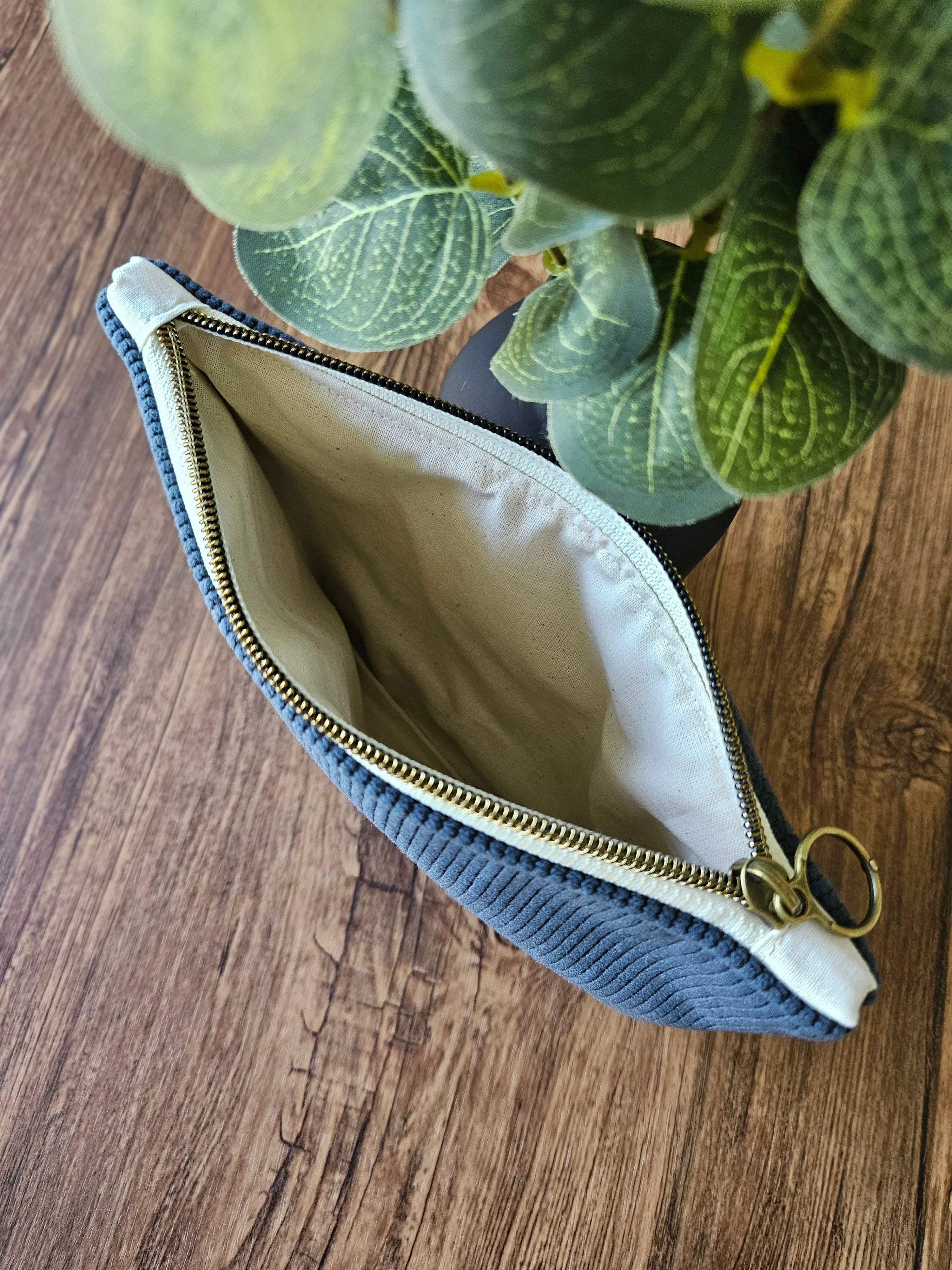 Pochette zippée en tissu bleu clair posée sur table en bois, plante verte en arrière-plan