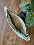 Trousse zippée en tissu beige et bleu, accessoire mode sur fond bois, plante décorative