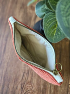 Pochette en tissu rose à fermeture éclair dorée, posée sur table en bois, plante verte à côté