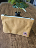 Pochette en velours côtelé beige avec fermeture éclair, poser sur une table en bois, accessoire mode tendance.