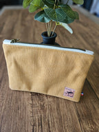 Pochette en velours côtelé beige avec fermeture éclair, poser sur une table en bois, accessoire mode tendance.