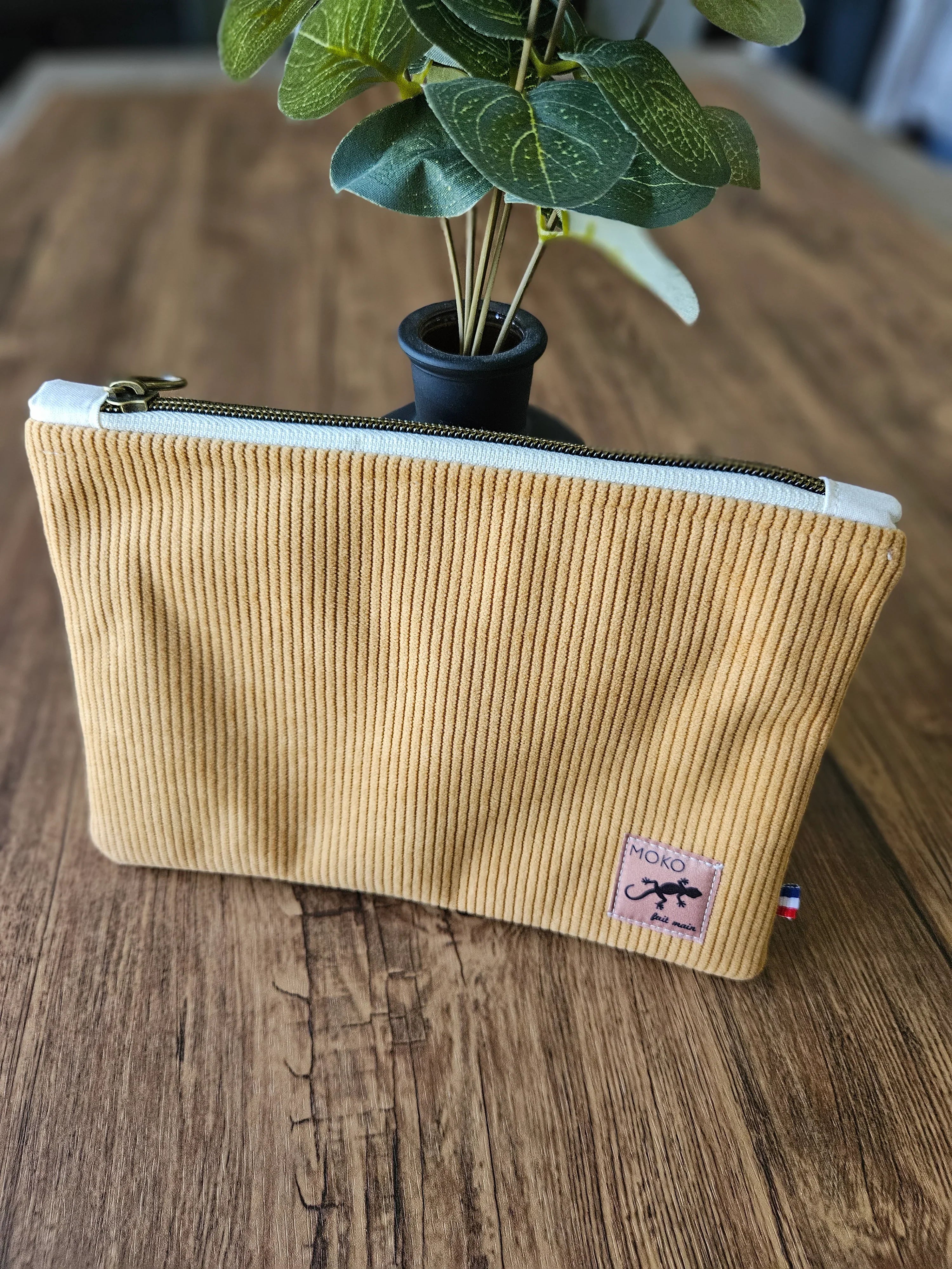 Pochette en velours côtelé beige avec fermeture éclair, poser sur une table en bois, accessoire mode tendance.