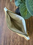 Pochette en tissu beige ouverte avec fermeture éclair dorée sur une table en bois
