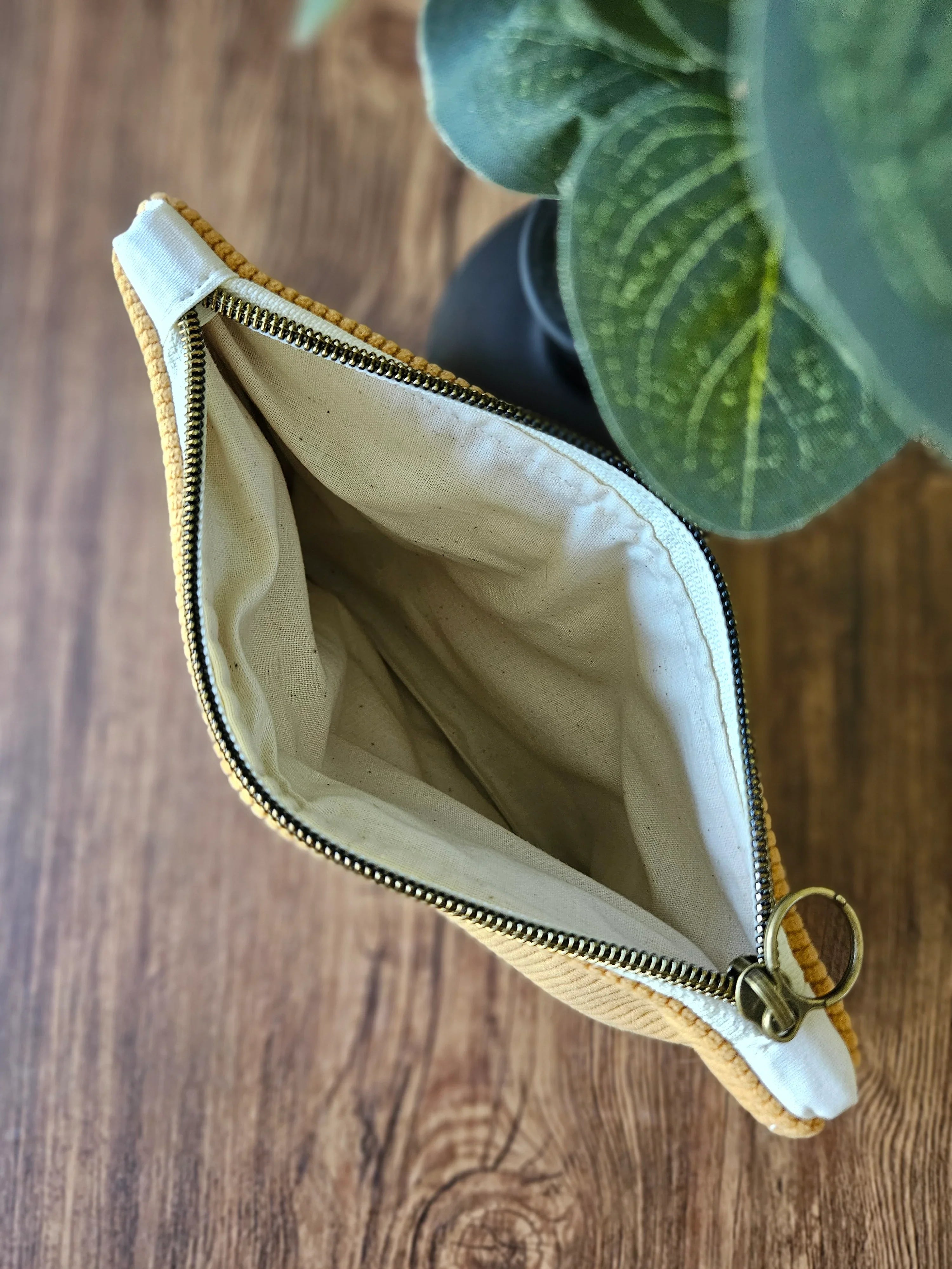 Pochette en tissu beige ouverte avec fermeture éclair dorée sur une table en bois