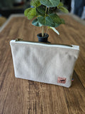 Pochette beige en velours à fermeture éclair, posée sur une table en bois, accessoire tendance.