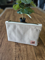 Pochette beige en velours à fermeture éclair, posée sur une table en bois, accessoire tendance.