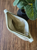 Pochette en tissu beige avec fermeture éclair dorée sur une table en bois, plante en arrière-plan